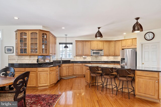 kitchen with sink, tasteful backsplash, hanging light fixtures, light hardwood / wood-style flooring, and stainless steel appliances