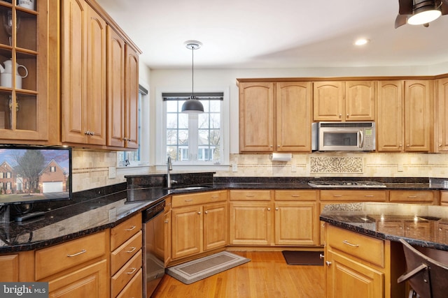 kitchen with sink, stainless steel appliances, decorative light fixtures, dark stone counters, and light wood-type flooring