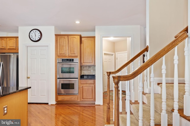 kitchen with tasteful backsplash, appliances with stainless steel finishes, dark stone countertops, and light hardwood / wood-style flooring