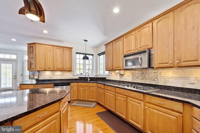 kitchen featuring appliances with stainless steel finishes, decorative light fixtures, dark stone countertops, backsplash, and light hardwood / wood-style flooring