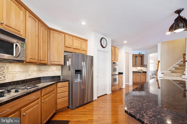 kitchen with stainless steel appliances, light hardwood / wood-style flooring, decorative backsplash, and dark stone counters