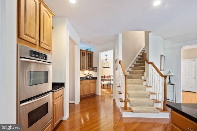 kitchen with dark stone countertops, decorative columns, light hardwood / wood-style floors, and stainless steel double oven