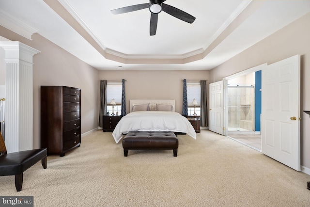 carpeted bedroom with a tray ceiling, ensuite bath, ornamental molding, and ceiling fan