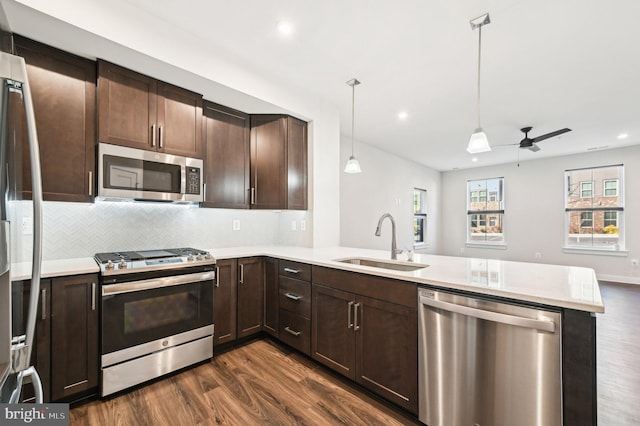 kitchen featuring hanging light fixtures, dark hardwood / wood-style floors, kitchen peninsula, appliances with stainless steel finishes, and sink