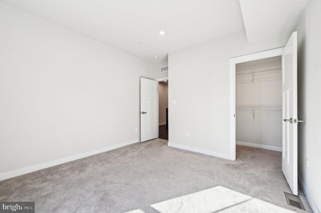 unfurnished bedroom featuring a closet, a spacious closet, and light carpet