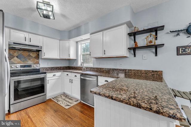 kitchen with appliances with stainless steel finishes, white cabinets, light wood-type flooring, and kitchen peninsula