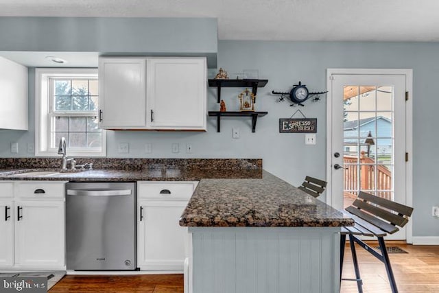 kitchen with sink, hardwood / wood-style floors, white cabinets, stainless steel dishwasher, and dark stone counters