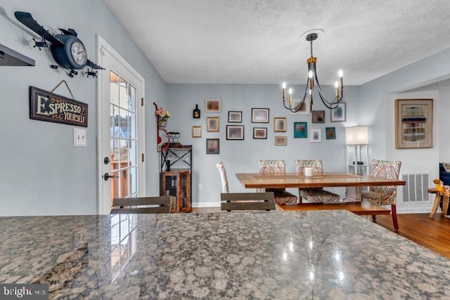 dining area with an inviting chandelier, a textured ceiling, and hardwood / wood-style flooring