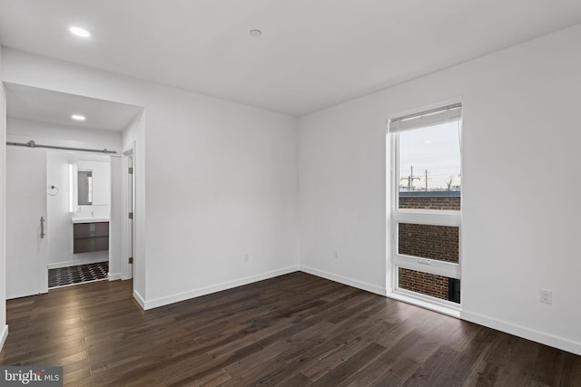 empty room with a barn door and dark hardwood / wood-style flooring