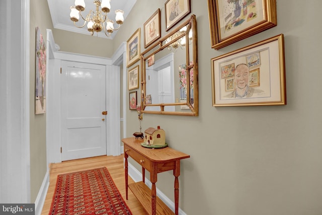 doorway with an inviting chandelier, ornamental molding, and light hardwood / wood-style floors