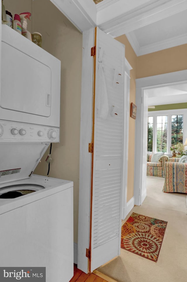 laundry area with crown molding, stacked washer / drying machine, and light carpet