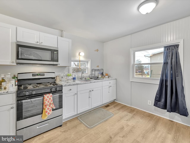 kitchen featuring white cabinetry, appliances with stainless steel finishes, light wood-type flooring, and plenty of natural light