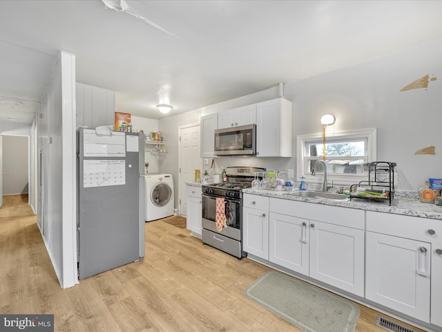 kitchen featuring sink, appliances with stainless steel finishes, white cabinetry, light hardwood / wood-style floors, and washer / dryer