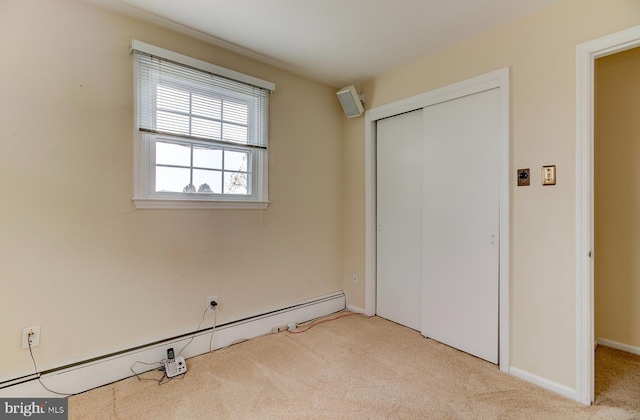 unfurnished bedroom featuring baseboard heating, a closet, and light carpet