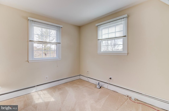 spare room featuring a baseboard heating unit, a healthy amount of sunlight, and light colored carpet