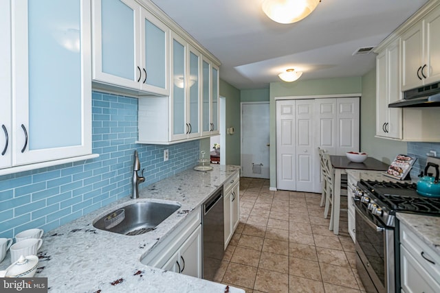 kitchen with appliances with stainless steel finishes, sink, white cabinets, decorative backsplash, and light stone countertops