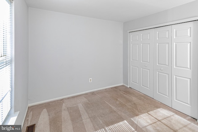 unfurnished bedroom with light carpet, multiple windows, and a closet