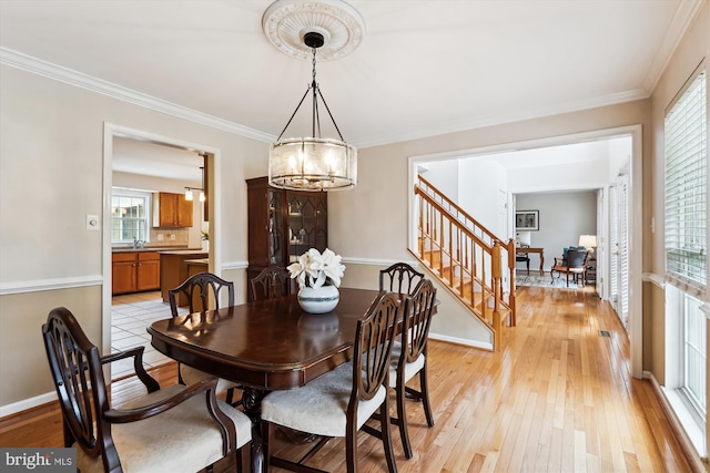 dining room featuring a chandelier, light wood finished floors, stairs, and crown molding