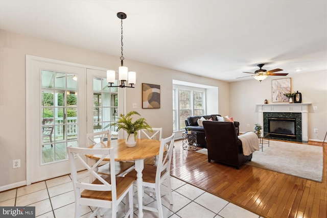 dining room featuring light tile patterned flooring, ceiling fan with notable chandelier, baseboards, and a high end fireplace