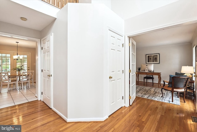 corridor with a notable chandelier, light wood-style flooring, visible vents, and baseboards