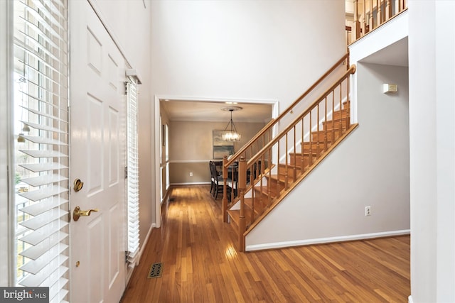 entryway with hardwood / wood-style floors, a chandelier, a towering ceiling, and stairs