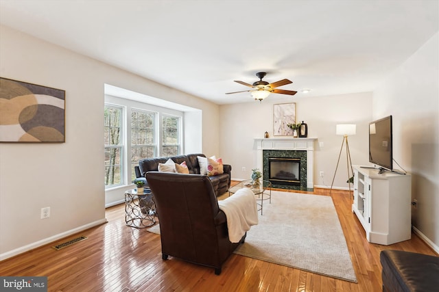 living room with a high end fireplace, visible vents, light wood-style flooring, and ceiling fan