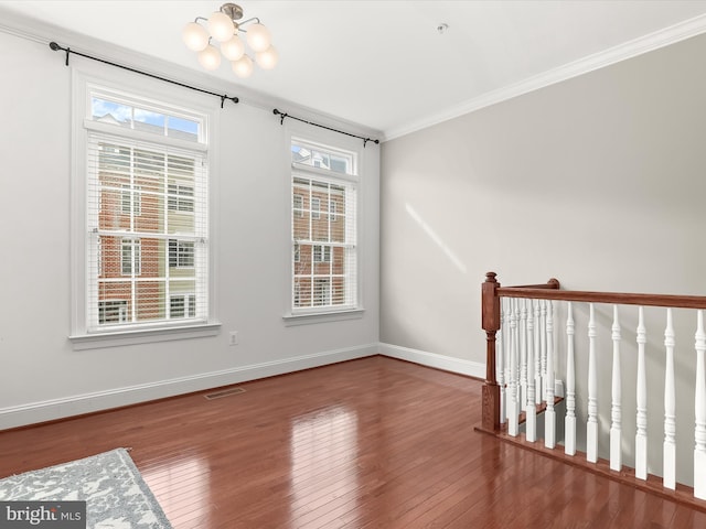 spare room featuring crown molding, wood-type flooring, and a chandelier