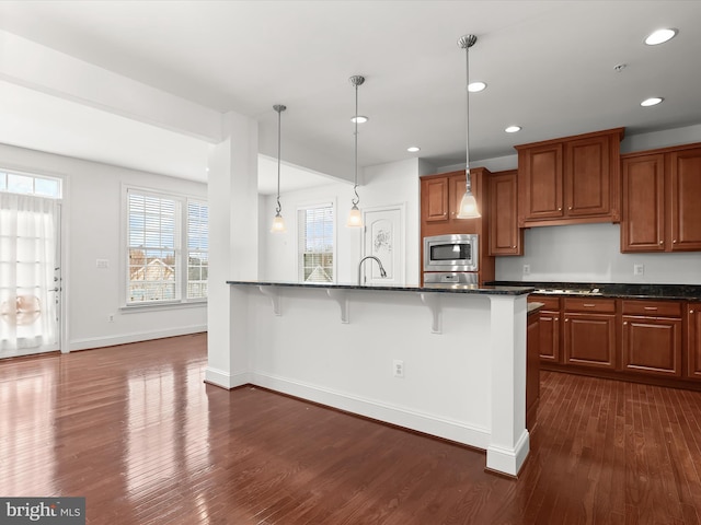 kitchen with a breakfast bar area, hanging light fixtures, dark stone countertops, dark hardwood / wood-style floors, and stainless steel appliances