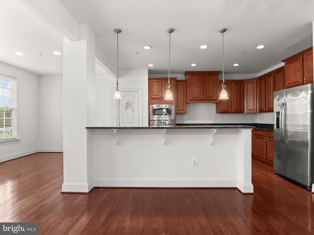 kitchen featuring stainless steel appliances, decorative light fixtures, dark hardwood / wood-style flooring, and a breakfast bar area