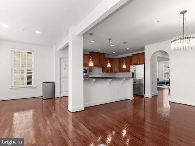 kitchen with dark wood-type flooring, stainless steel appliances, a breakfast bar, and hanging light fixtures