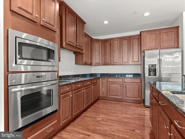 kitchen with appliances with stainless steel finishes, light wood-type flooring, and dark stone counters