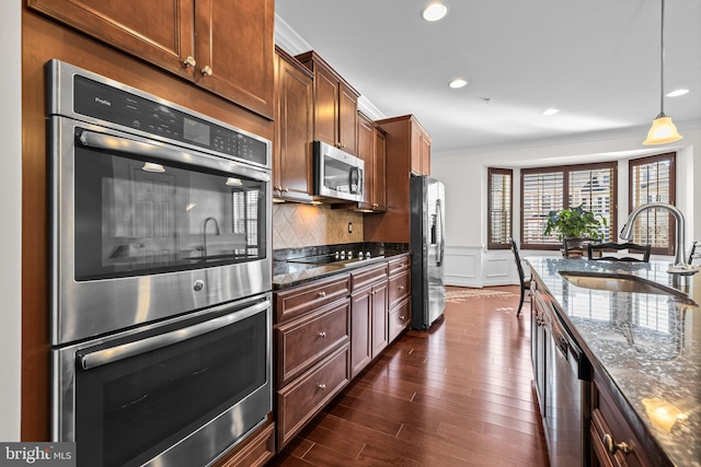 kitchen with crown molding, pendant lighting, stainless steel appliances, and dark stone countertops