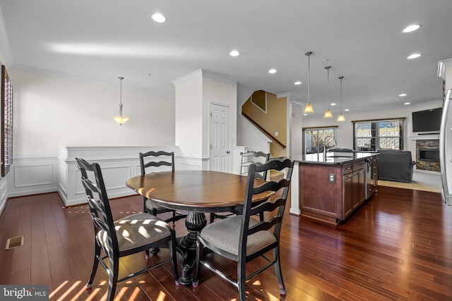 dining space featuring ornamental molding, a wainscoted wall, dark wood-type flooring, and a fireplace