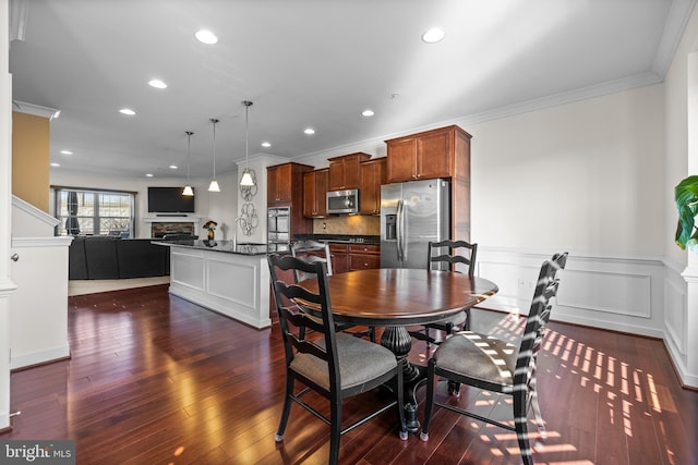 dining space featuring dark wood-style flooring, crown molding, a fireplace, recessed lighting, and wainscoting