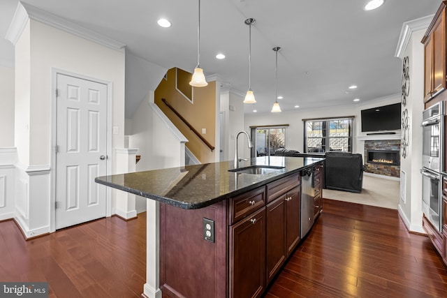 kitchen with a center island with sink, open floor plan, dark stone countertops, hanging light fixtures, and a sink