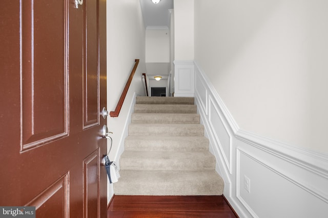 stairs with ornamental molding, wainscoting, wood finished floors, and a decorative wall