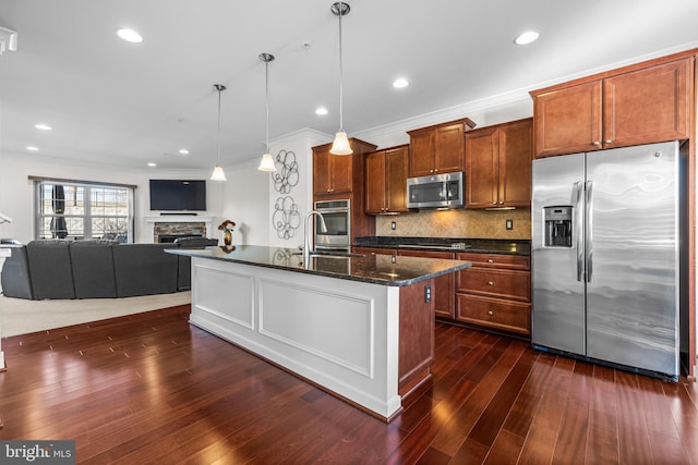 kitchen with stainless steel appliances, open floor plan, hanging light fixtures, brown cabinetry, and a center island with sink