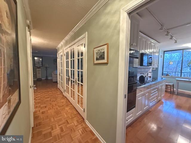 corridor featuring rail lighting, ornamental molding, french doors, and light parquet floors