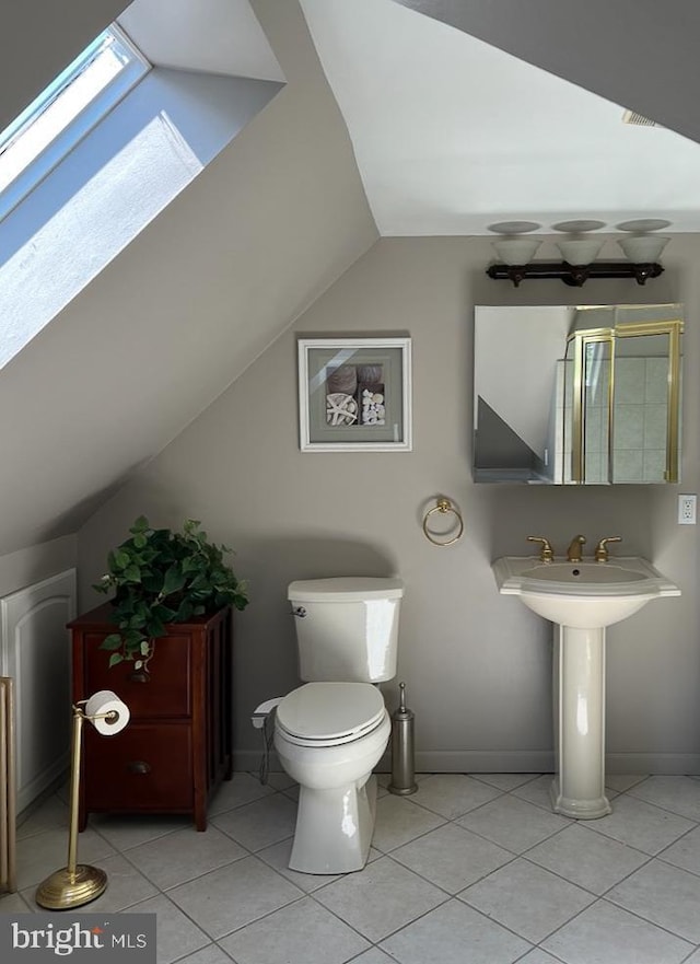 bathroom with sink, vaulted ceiling with skylight, tile patterned floors, and toilet