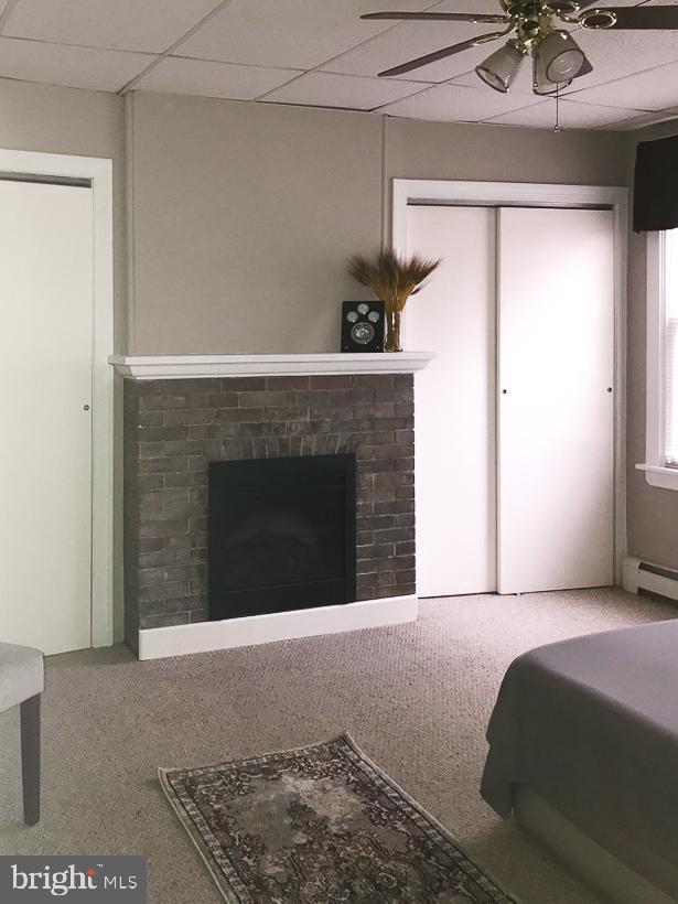 carpeted bedroom with a baseboard radiator, a closet, ceiling fan, a fireplace, and a drop ceiling