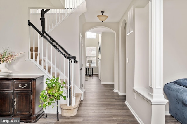 foyer with baseboards, arched walkways, wood finished floors, and stairway