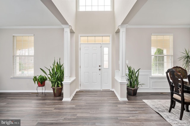 foyer with a decorative wall, crown molding, ornate columns, and wood finished floors