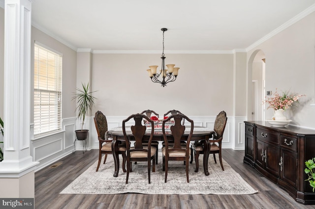 dining space with dark wood-type flooring, a wainscoted wall, ornamental molding, an inviting chandelier, and arched walkways