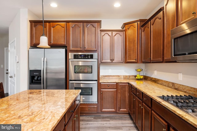 kitchen with light stone counters, wood finished floors, stainless steel appliances, and decorative light fixtures