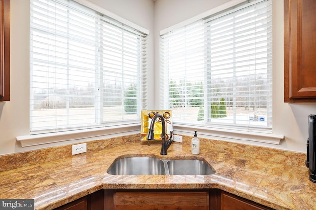 kitchen featuring brown cabinets, light stone countertops, and a sink