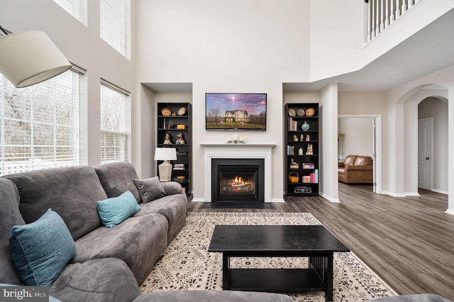 living room featuring a fireplace with flush hearth, wood finished floors, arched walkways, and a healthy amount of sunlight