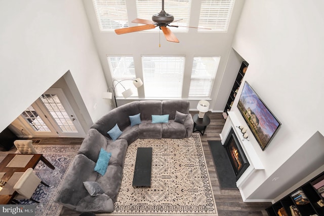 living room featuring baseboards, ceiling fan, a lit fireplace, a high ceiling, and wood finished floors