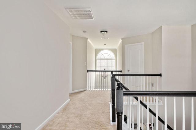 hall featuring visible vents, an upstairs landing, light colored carpet, and baseboards