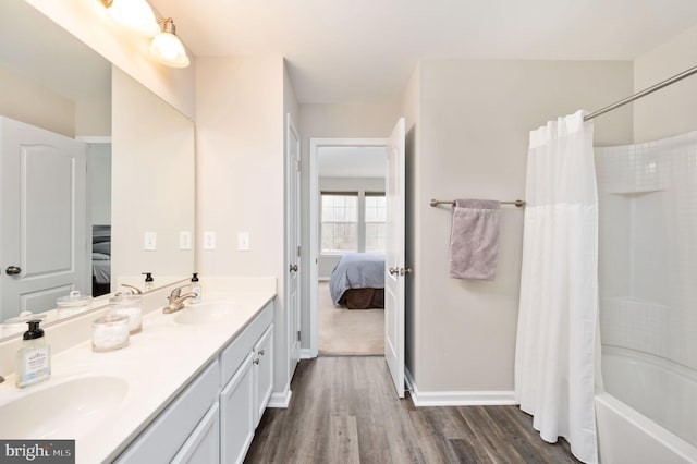 ensuite bathroom with double vanity, connected bathroom, wood finished floors, and a sink