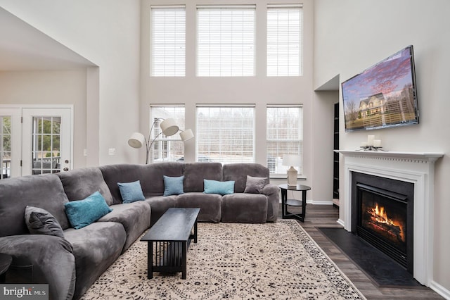 living room featuring a glass covered fireplace, a towering ceiling, dark wood finished floors, and a wealth of natural light